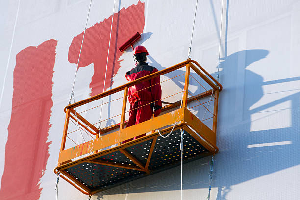Worker painting a large exterior wall on a ladder